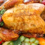 Whole turkey on a bed of grapes, apples, fresh herbs on a white platter