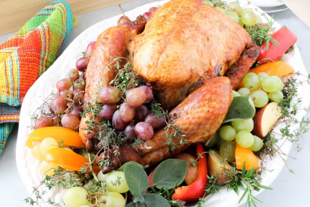 Whole bird on a bed of grapes, apples, fresh herbs on a white platter