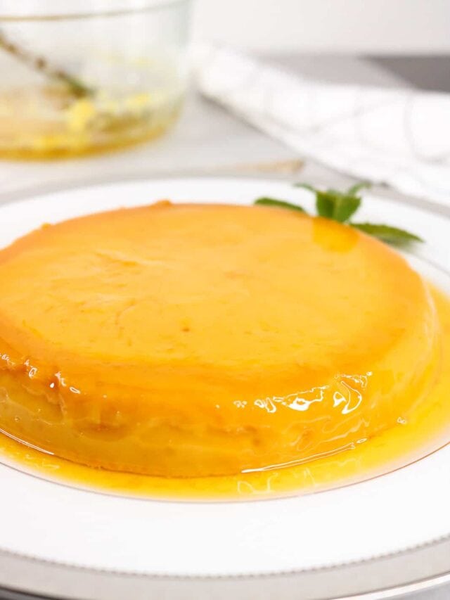 Instant pot flan on white plate with syrup around the flan. Mint leaves on the side and bowl in the background