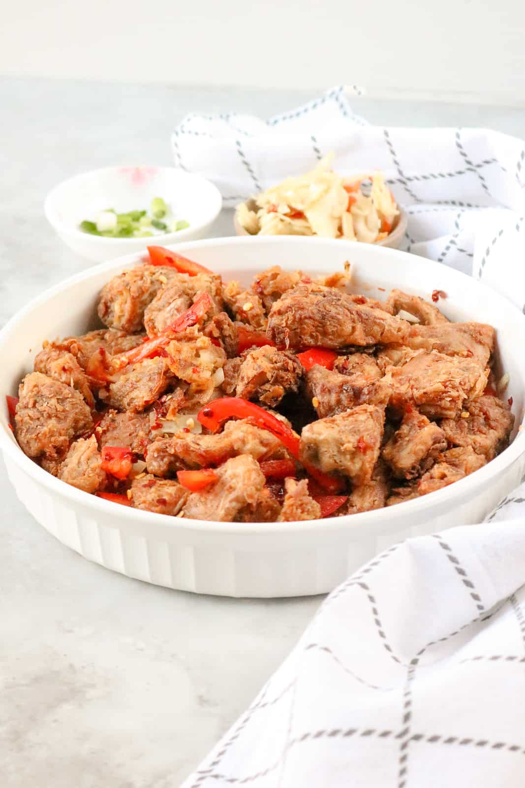 Haitian Griot in white bowl topped with peppers and pickliz in the background