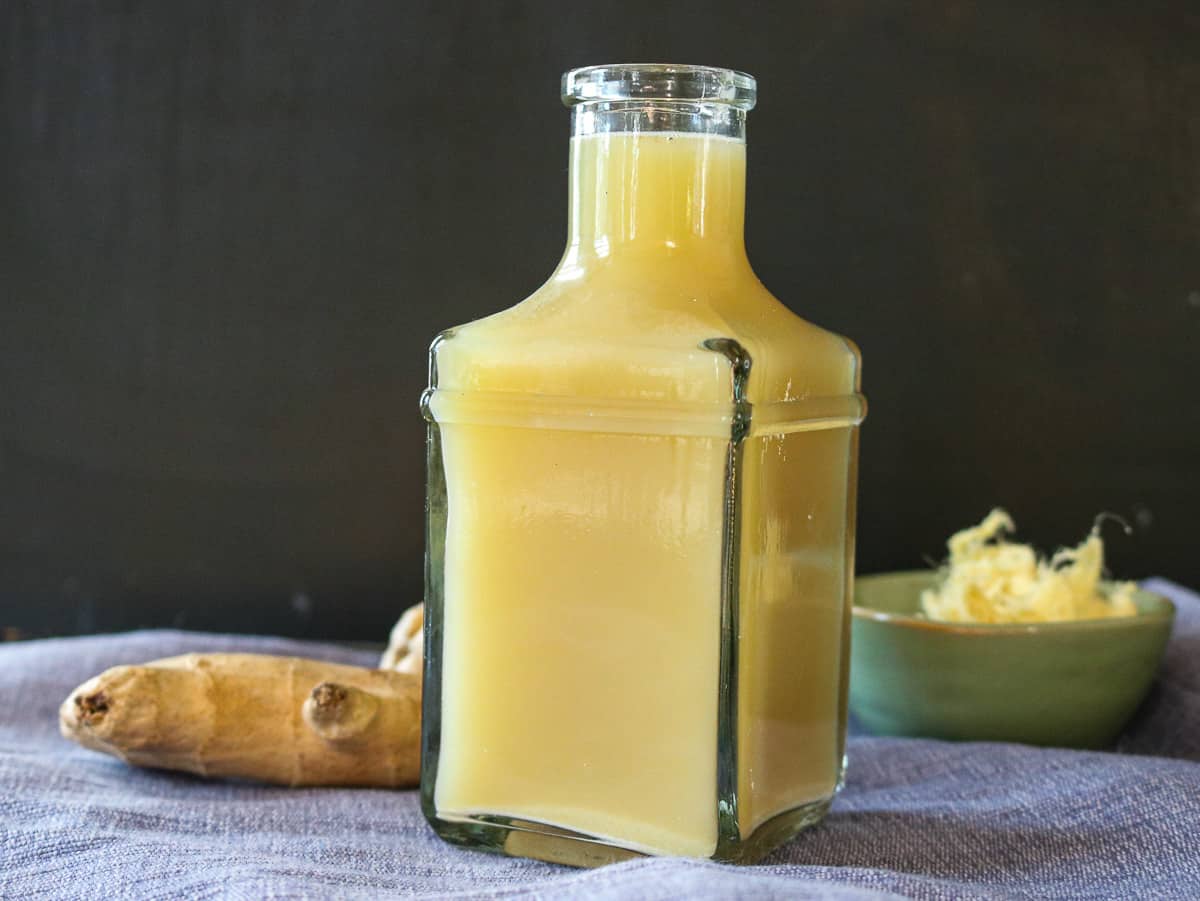 quick and easy ginger juice without a juicer. ginger tea in clear bottle with ginger in the background