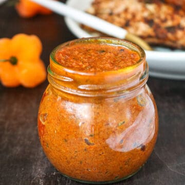 Shito in glass jar with habanero peppers in the back with fish on white plate