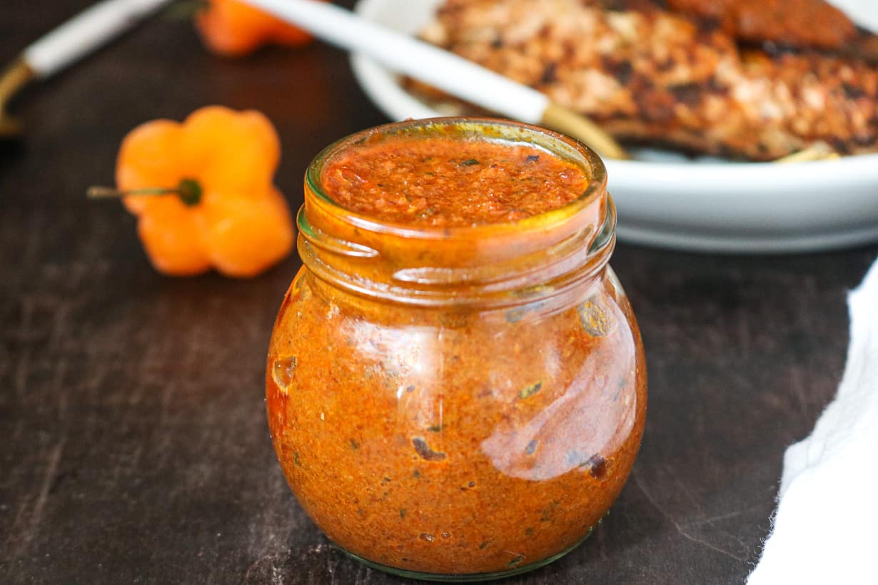 Shito in glass jar with habanero peppers in the back with fish on white plate