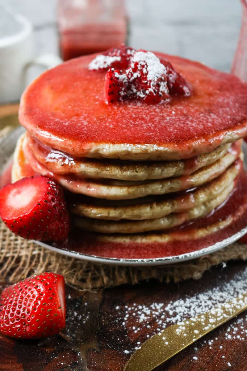stack of pancakes topped with strawberries and syrup