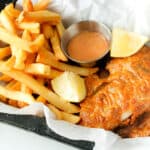 fish and fries with lemon wedges on top of parchment paper