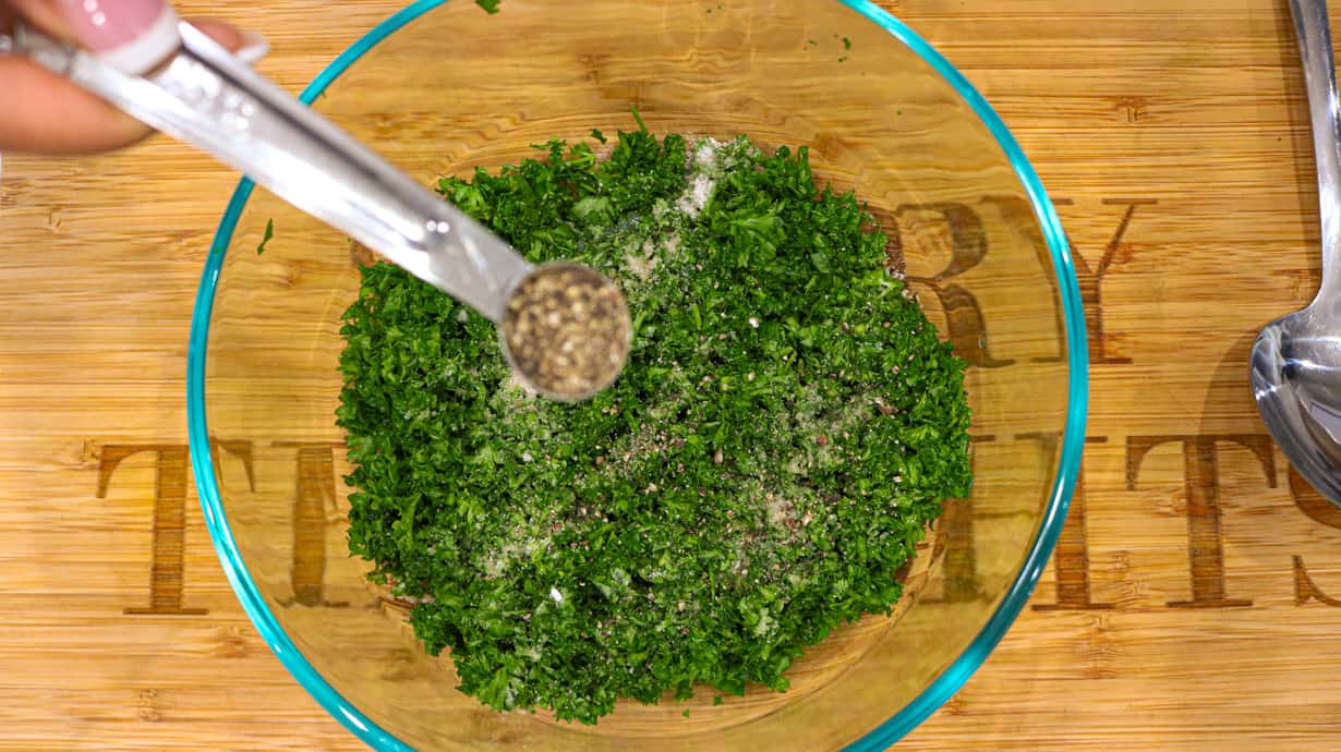 black pepper being added to herbs