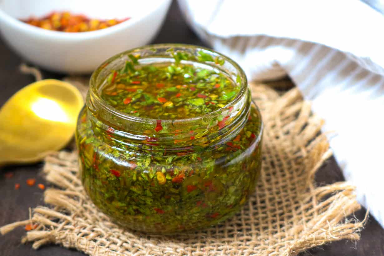 CHIMICHURRI SAUCE in glass jar with peppers in white bowl