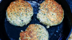 3 salmon burgers cooking in skillet