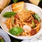 Haitian spaghetti topped with peppers, basil, and onions on white bowl