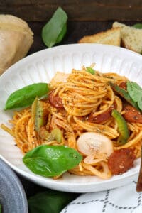Haitian spaghetti topped with peppers, basil, and onions on white bowl