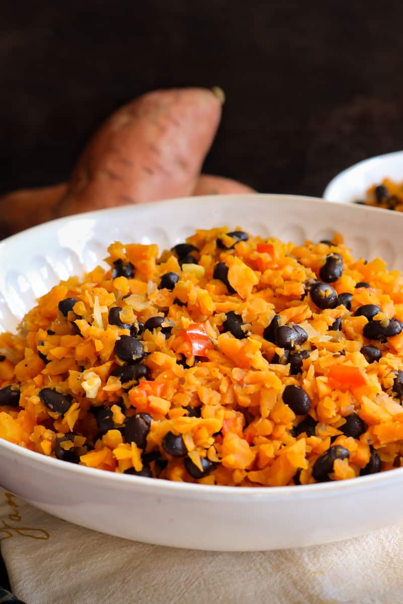 vertical view of sweet potato rice in white bowl and raw sweet potatoes in the back