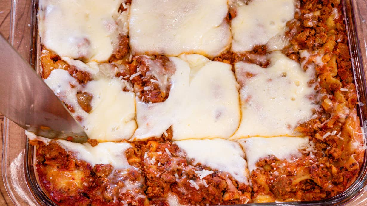lasagna in baking dish with knife cutting the lasagna