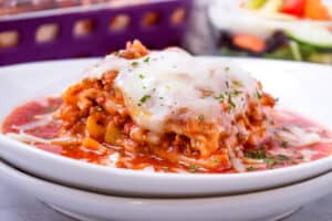 closeup view of lasagna on double plate toped with parsley flakes and cheese