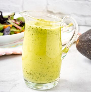 avocado Green Goddess Dressing in clear jar with salad and avocado in the back