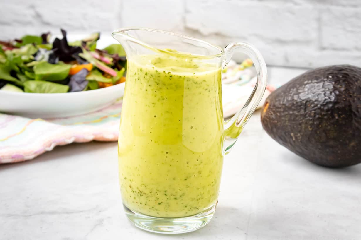 avocado Green Goddess Dressing in clear jar with salad and avocado in the back