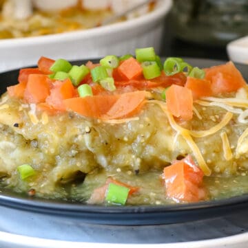 enchilada on black plate topped with green onions and tomatoes