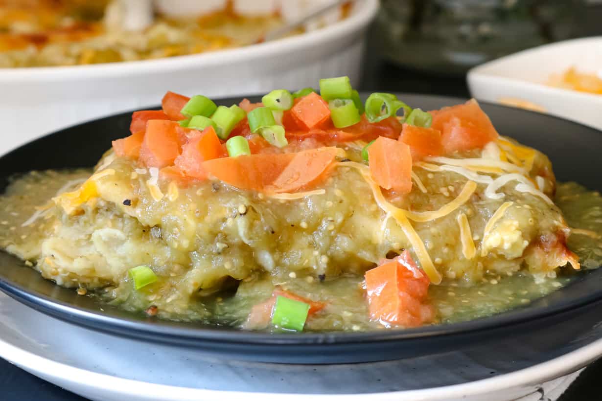 enchilada on black plate topped with green onions and tomatoes