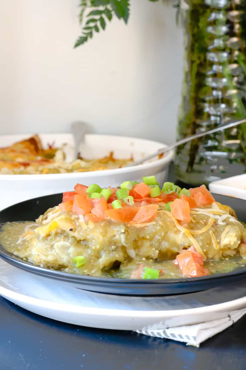 enchilada on black plate topped with green onions and tomatoes