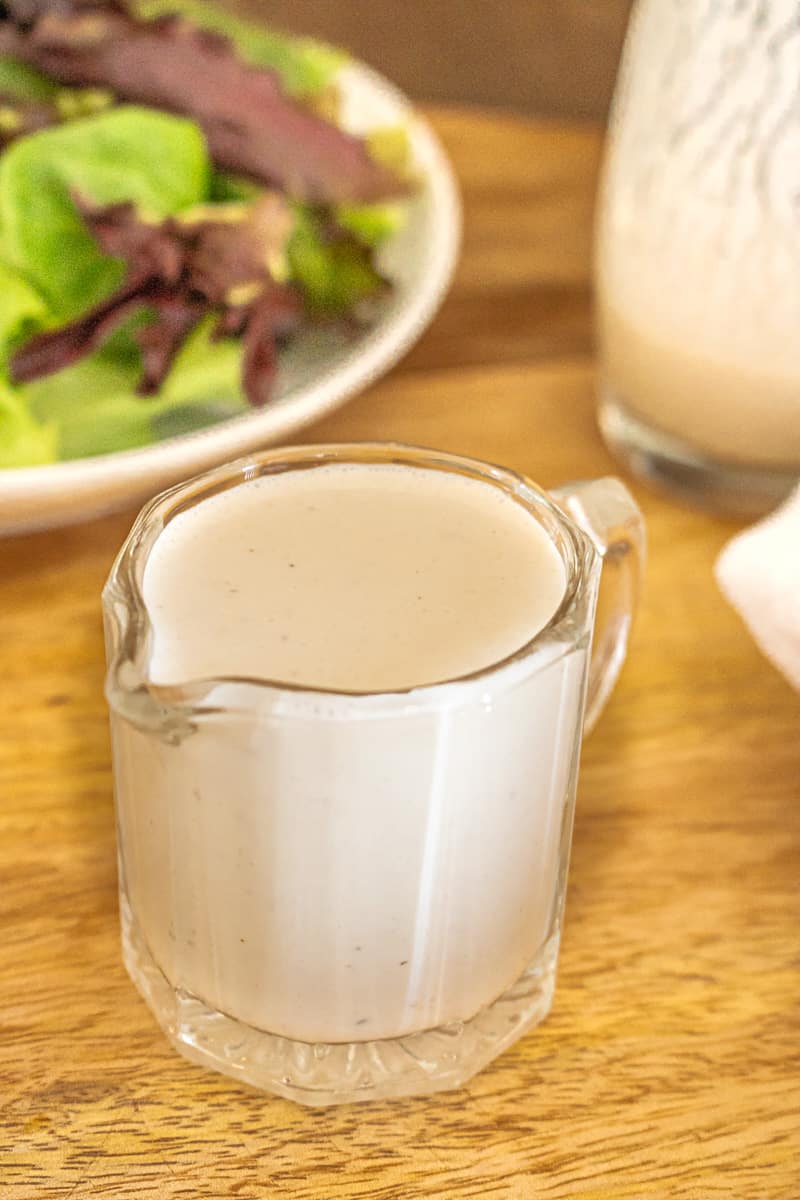 Salad dressing in glass container with salad in the background