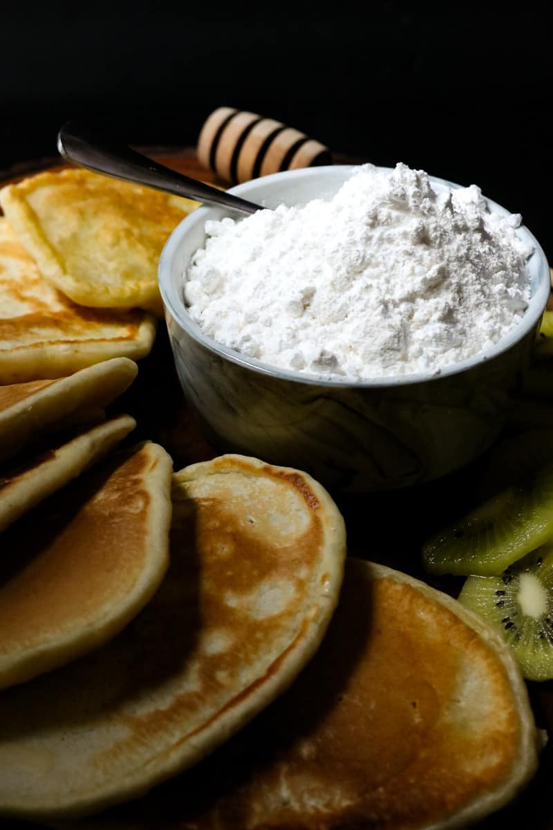 powdered sugar in bowl with spoon and pancakes