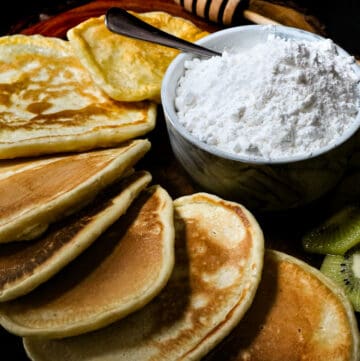 powdered sugar in bowl with spoon and pancakes