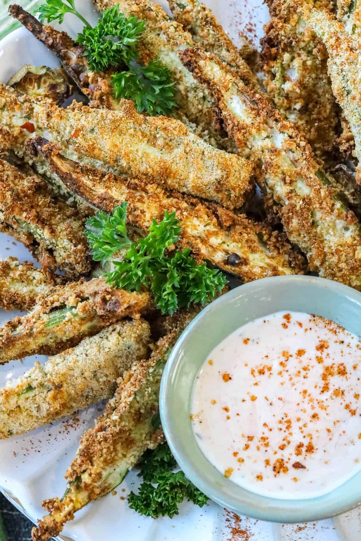 air fryer okra on white plate with fresh parsley and dipping sauce.