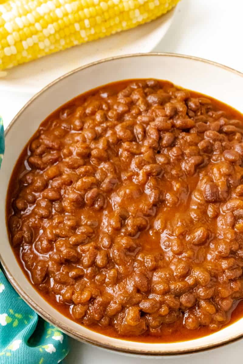 baked beans in brown bowl with corn in the background