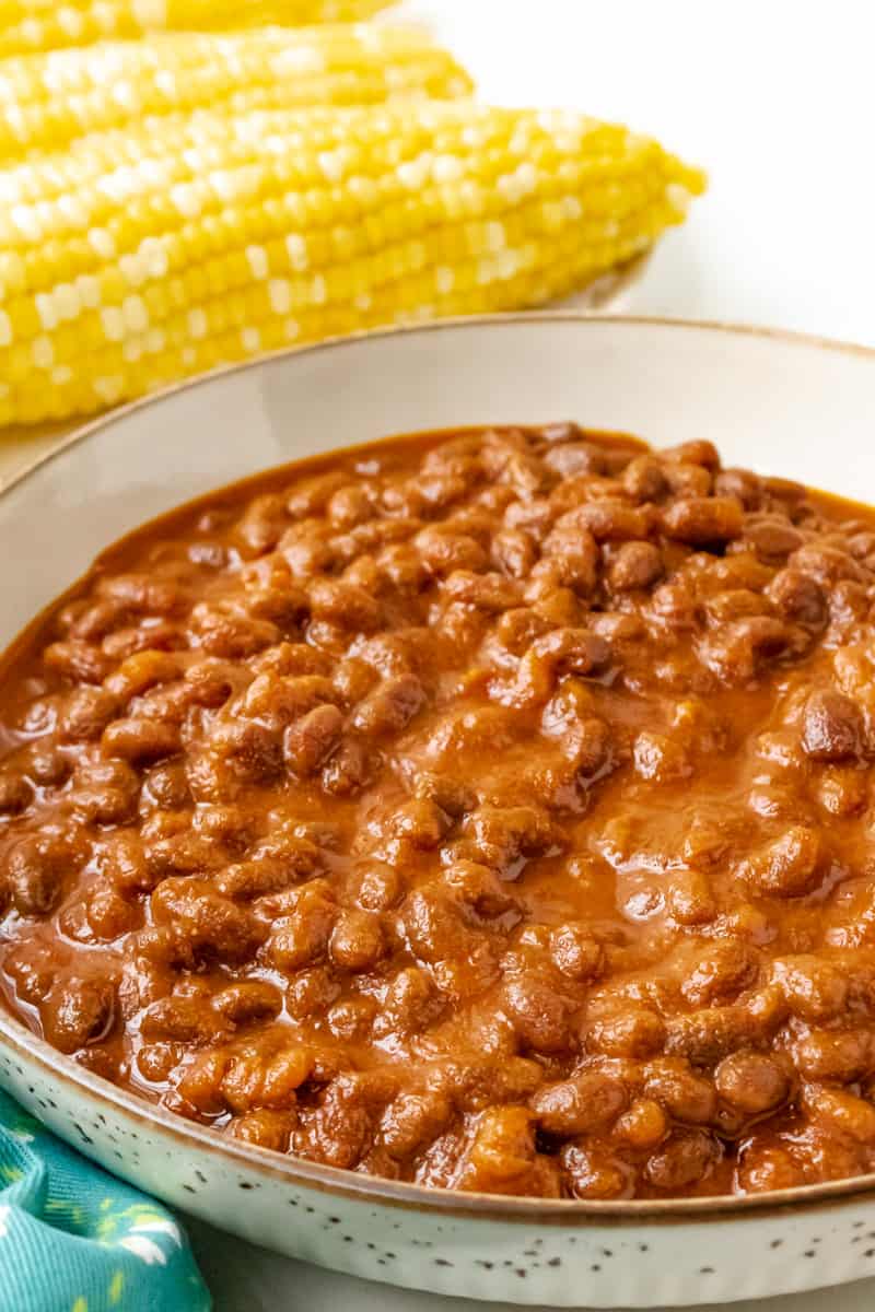 baked beans in brown bowl with corn in the background