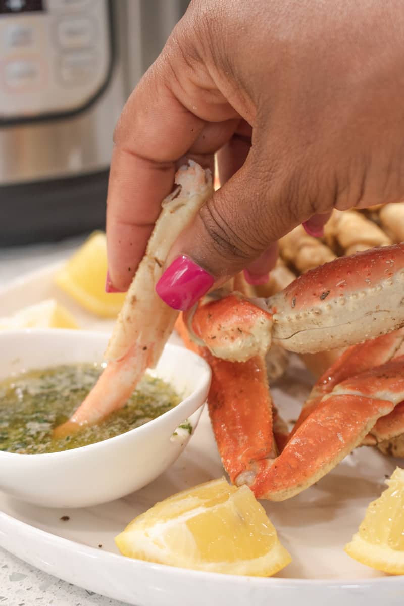 Hand holding crab meat in garlic butter dipping sauce. 5-minute, succulent, fast, and enjoyable instant pot crab legs with an irresistible butter garlic sauce. Perfect for the summer outings! #instantpotcrablegs #garlicbuttersauce #crablegs #snowcrablegs #savorythoughts