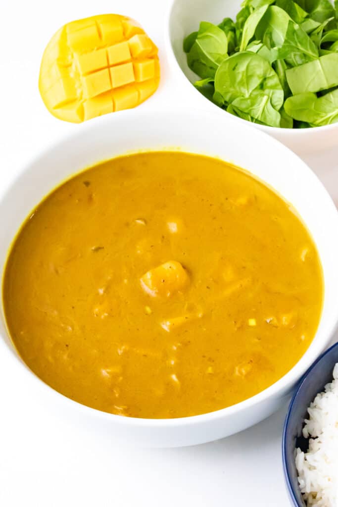 vertical view of mango curry with spinach and mango and rice on white bowl