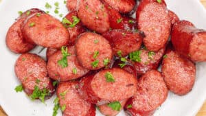 cooked air fryer sausage on white plate topped with fresh parsley flakes