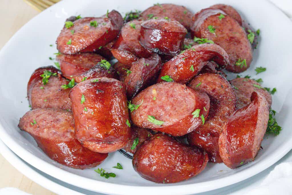 cooked air fryer sausage on white plate topped with fresh parsley flakes