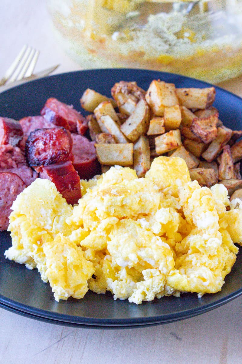 Scrambled eggs in air fryer on black plate with sausage and potatoes