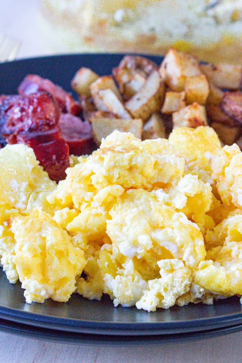 Scrambled eggs in air fryer on black plate with sausage and potatoes