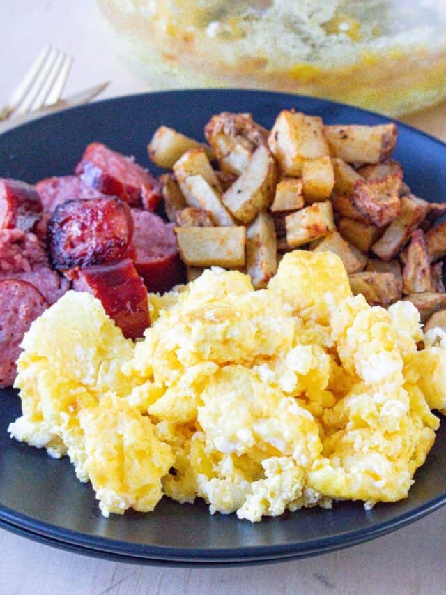 Scrambled eggs in air fryer on black plate with sausage and potatoes