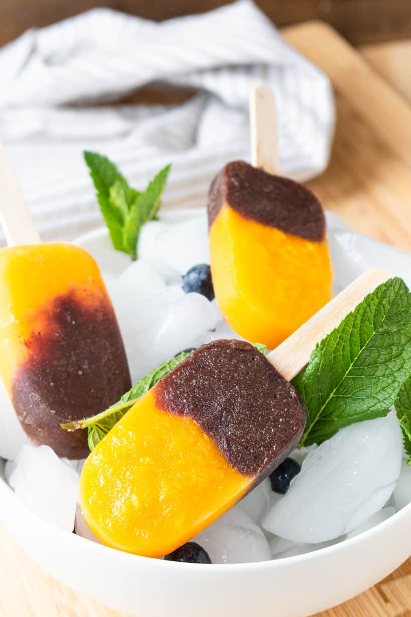 close up view of mango pops in bowl of ice with mint and blueberries