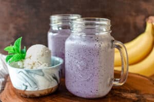 blueberry milkshake and ice cream on wooden board with banana in the back