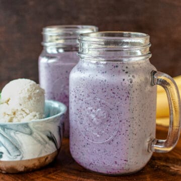 blueberry milkshake and ice cream on wooden board with banana in the back