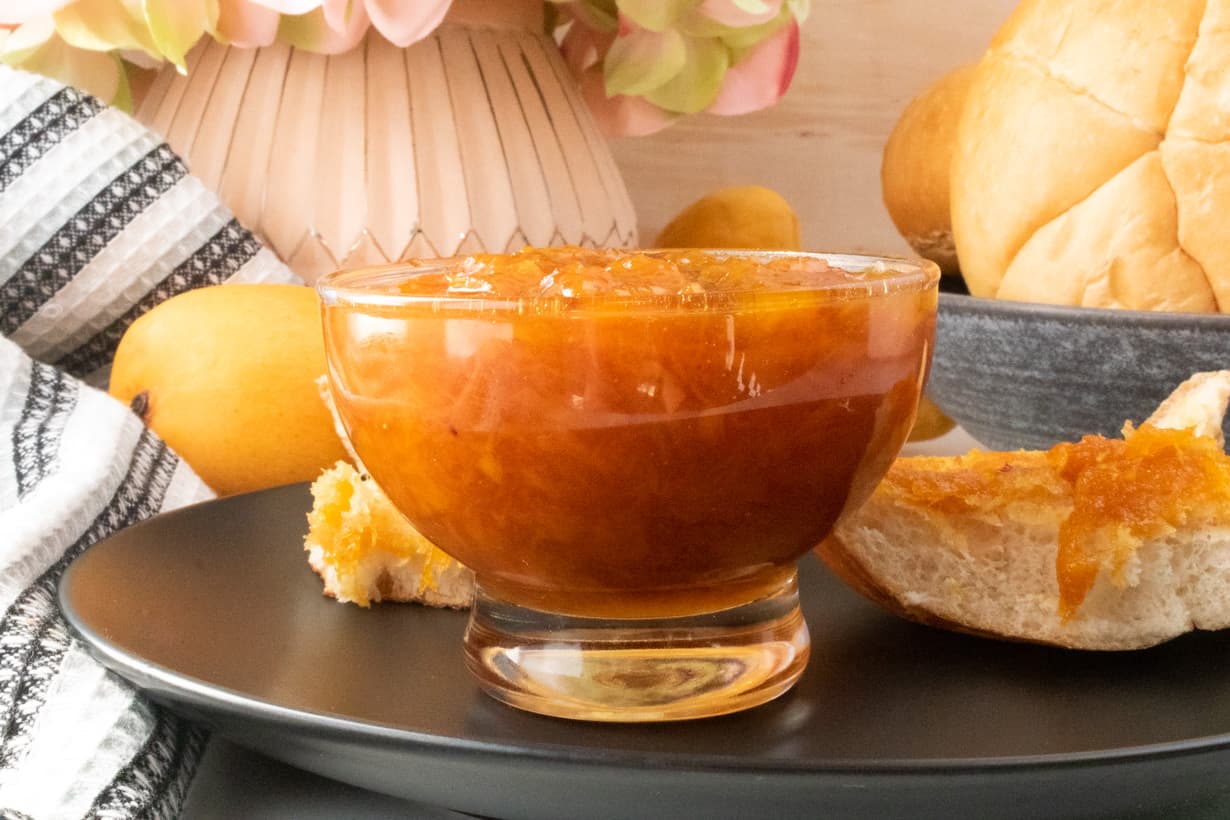mango jam in glass jar on black plate with bread, flower and mango in the background