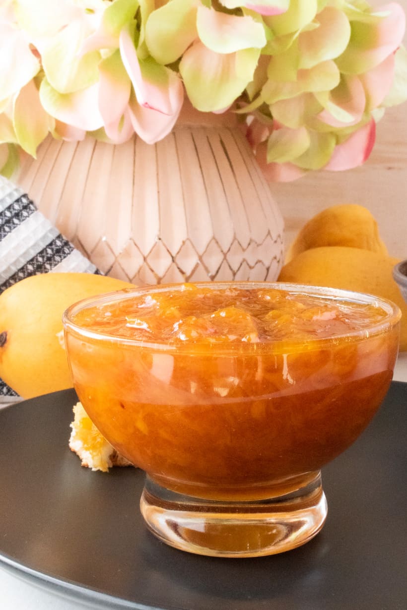 mango jam in glass jar on black plate with flower in the background and mangos