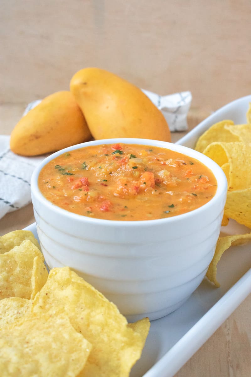 Mango salsa in white bowl with chips and mango and towel