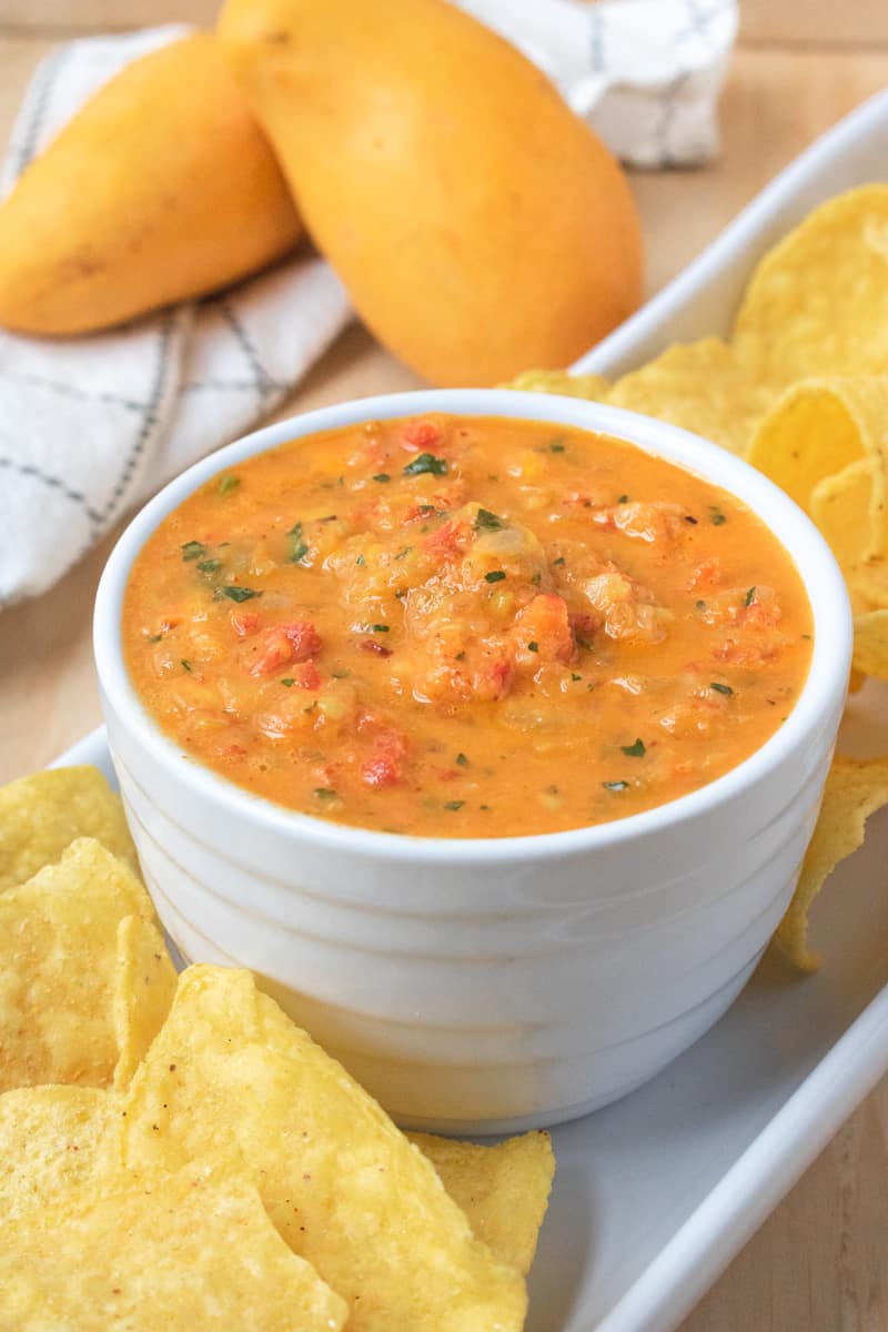 Mango salsa in white bowl with chips and mangos