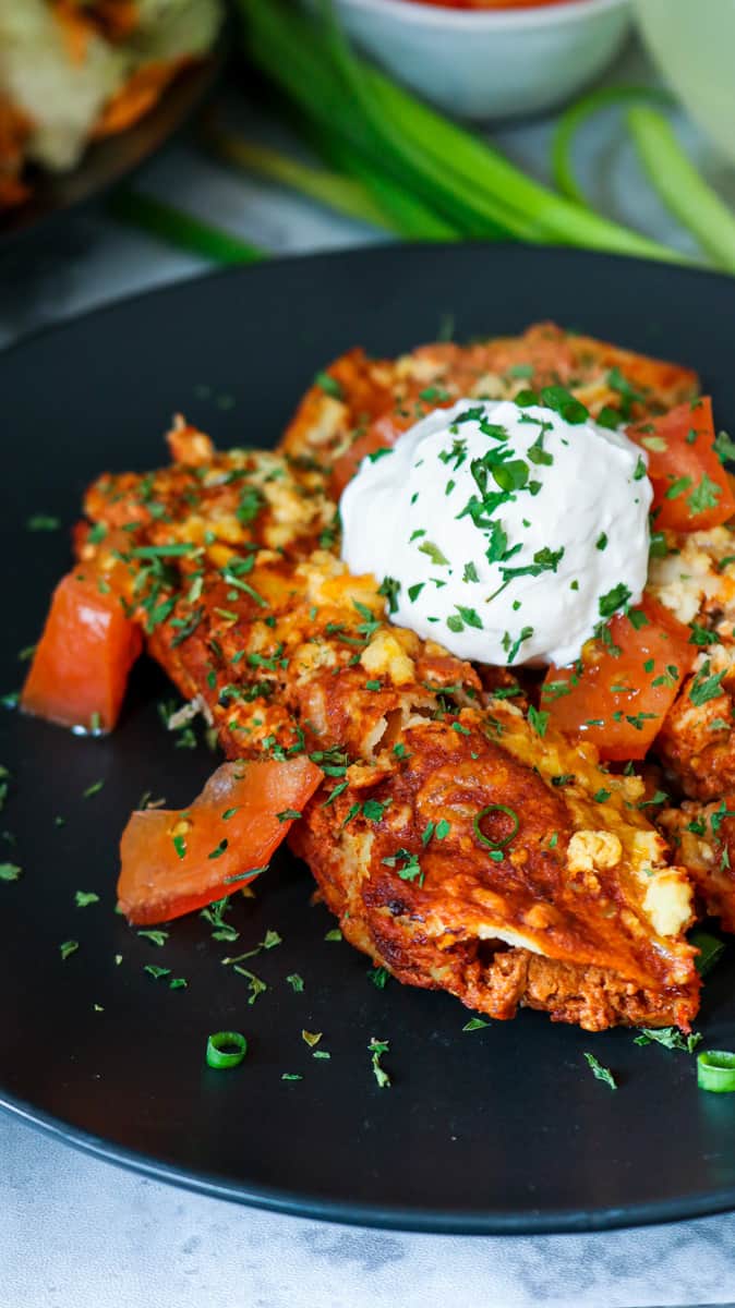 enchiladas on black plate topped with sour cream