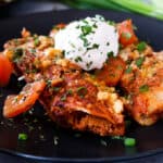 enchiladas on black plate topped with sour cream