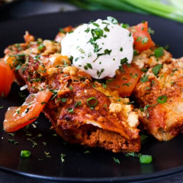 enchiladas on black plate topped with sour cream