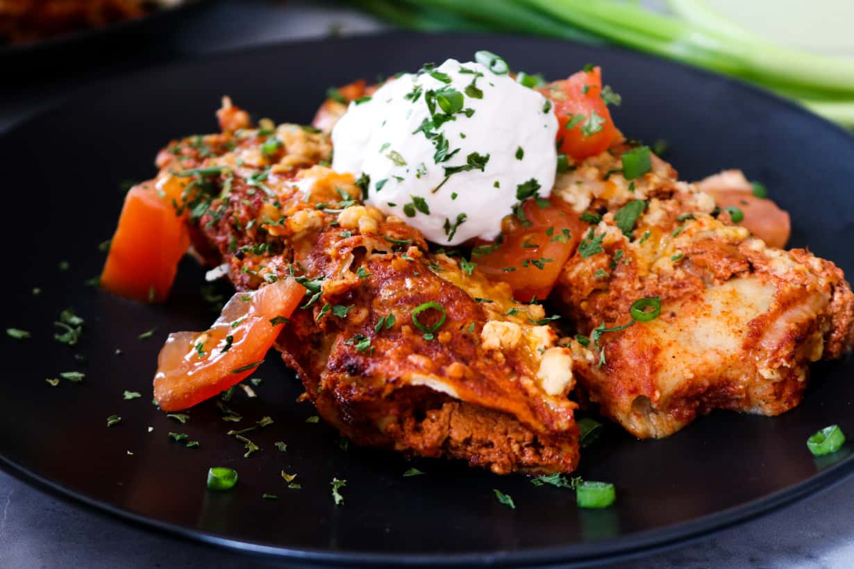 enchiladas on black plate topped with sour cream