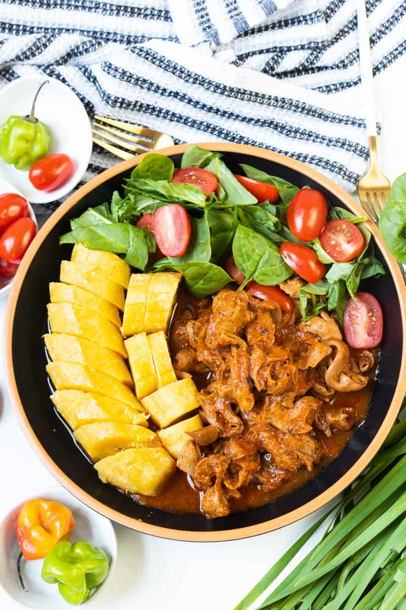 Haitian lambi in bowl with boiled plantains, spinach and tomatoes