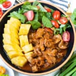 Haitian lambi (conch stew) in bowl and black bowl with boiled plantains, spinach, and tomatoes.