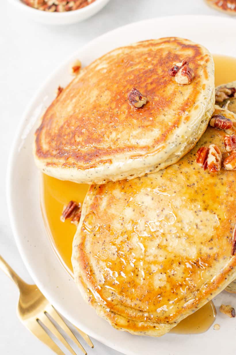 pancakes topped with maple syrup and pecans in white plate