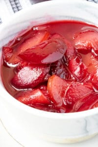 cooked plums in white bowl with gold rim